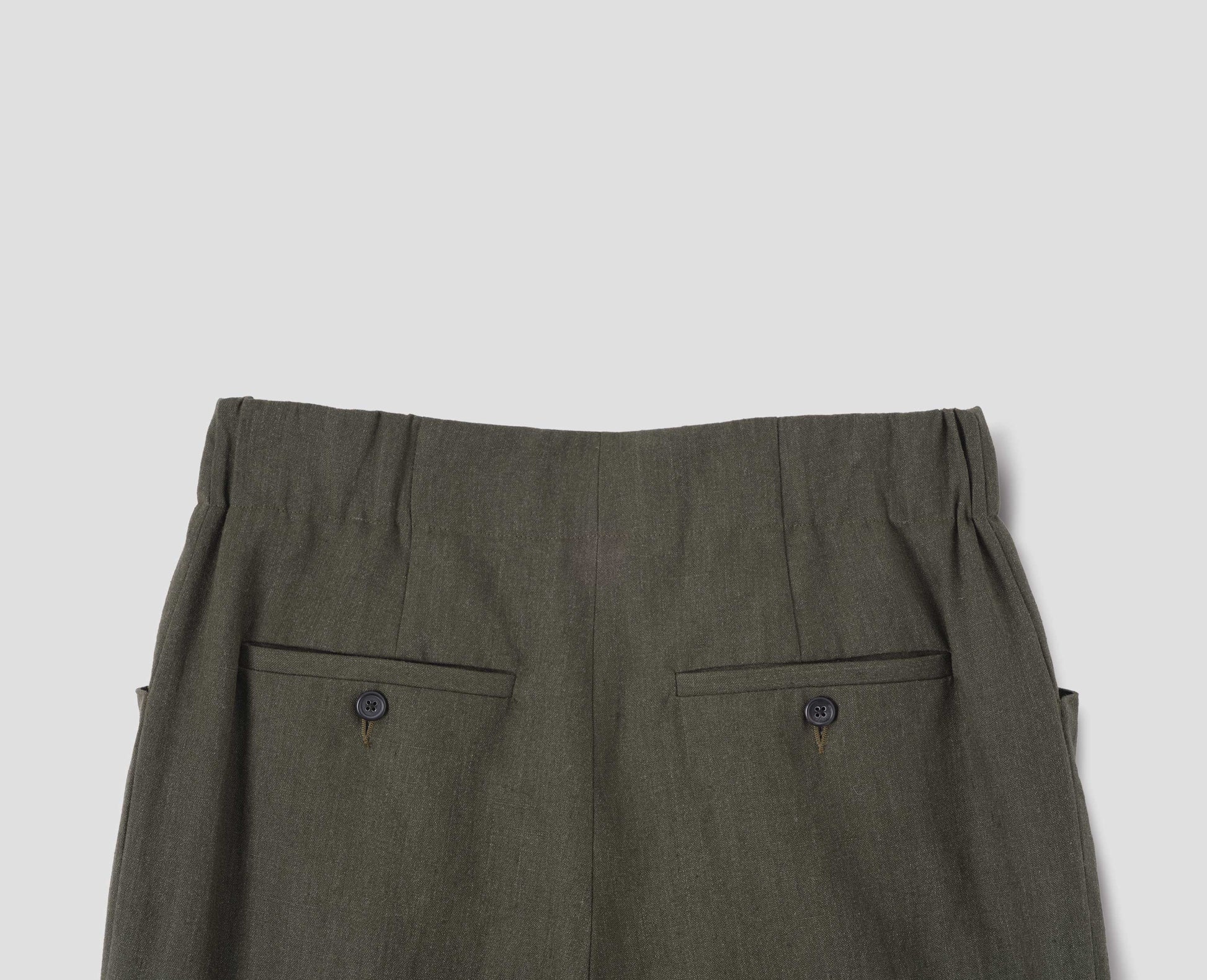 Dark green linen trousers with elasticated waistband and horn button-through jet back pockets. Back flat lay view.