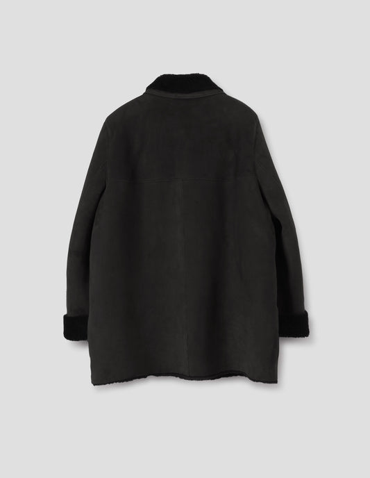 Black sheepskin coat with contrasting curly merino collar with narrow sueded binding, back yoke with centre back seam,  raw edges on contrasting curly merino turn-up cuffs and hem. Back flat lay view.