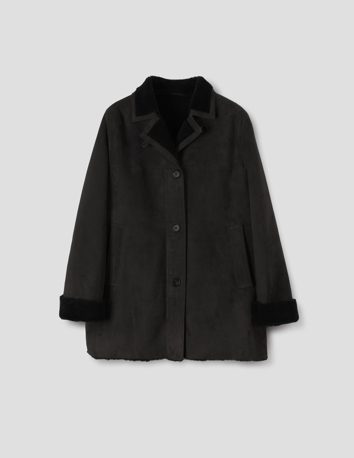 Black sheepskin coat with contrasting curly merino collar revere with narrow sueded binding, wide placket with button loop closure, horn button fastening, front yoke, slanted single welt front pockets, raw edges on contrasting curly merino turn-up cuffs and hem. Front flat lay view.
