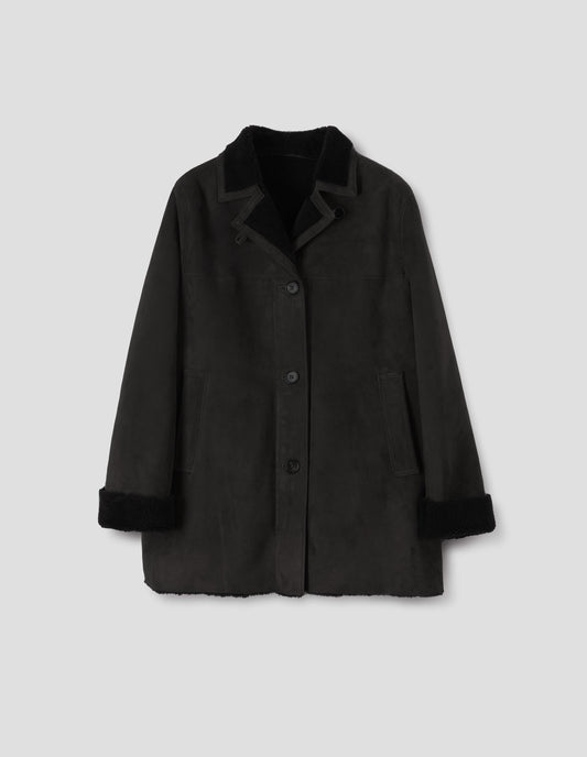 Black sheepskin coat with contrasting curly merino collar revere with narrow sueded binding, wide placket with button loop closure, horn button fastening, front yoke, slanted single welt front pockets, raw edges on contrasting curly merino turn-up cuffs and hem. Front flat lay view.