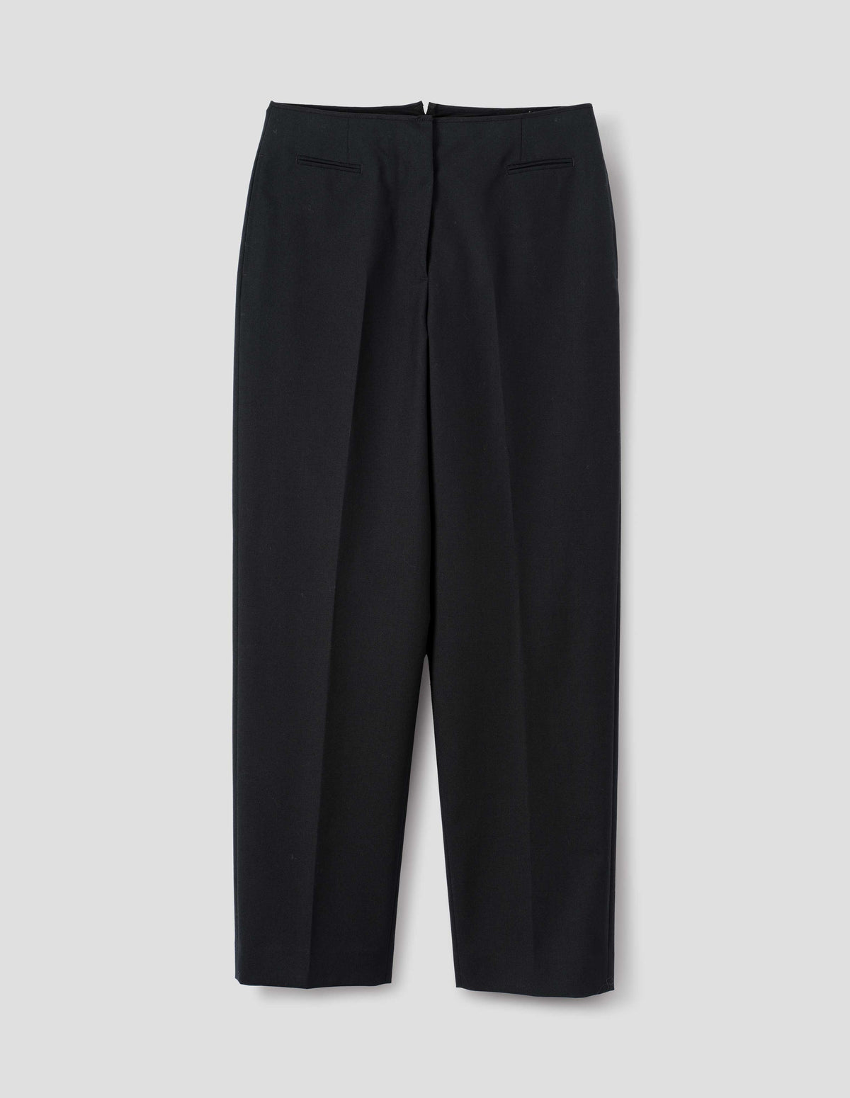 Black wool trousers with cotton fine-binding waistband, zip fly with hook and bar fastening, small front welt pockets and side pockets. Front flat lay view.