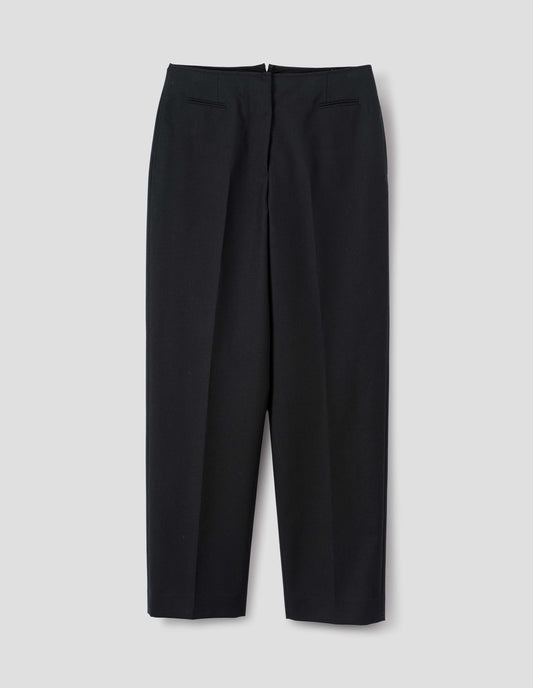 Black wool trousers with cotton fine-binding waistband, zip fly with hook and bar fastening, small front welt pockets and side pockets. Front flat lay view.