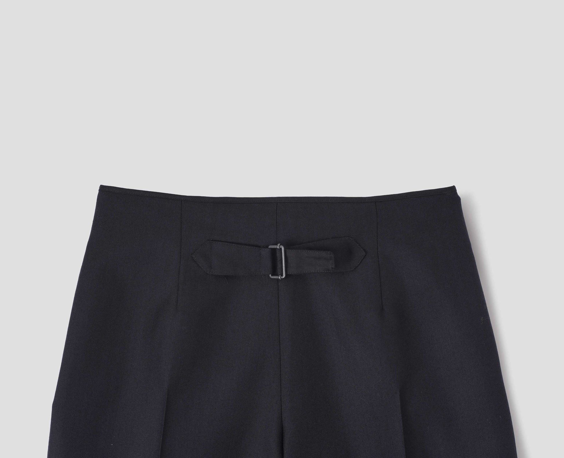 Dark blue wool trousers with cotton fine-binding waistband and cinch detail on back. Back flat lay view.