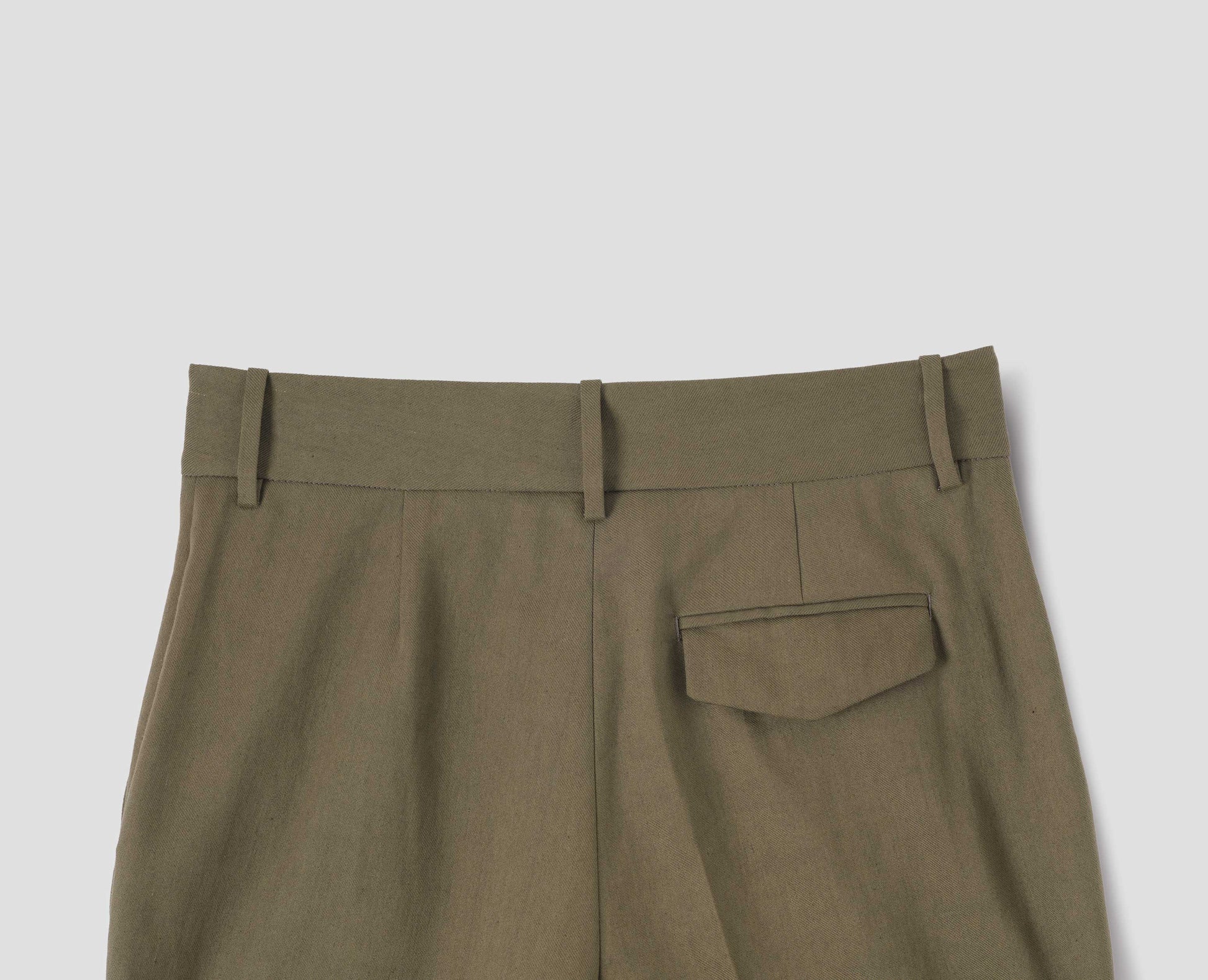Green cotton linen trousers with belt loops and concealed horn button-fastening flap back pocket. Back flat lay view.