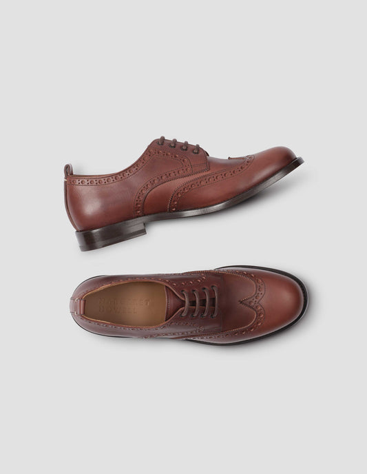A pair of brown leather brogues with heel pull detail and contrast leather lining. View from above flat lay view.