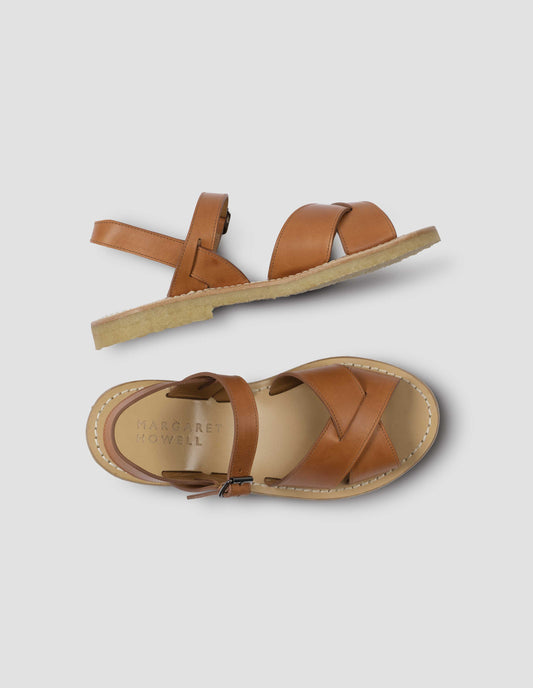 A pair of tan leather sandals with roller buckle fastening, contrast leather sole lining and crepe soles. View from above flat lay view.