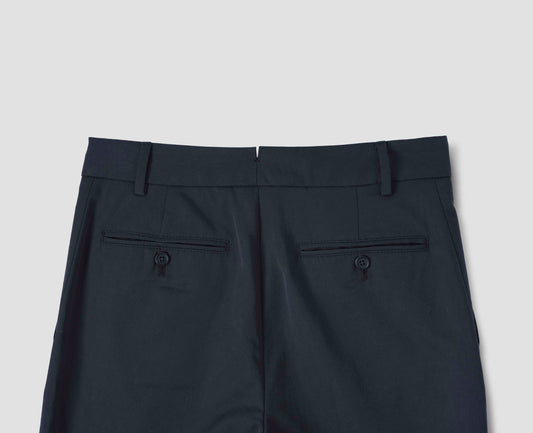Dark blue trousers with side pockets, belt loops and button-through welt back pockets, back flat lay view.