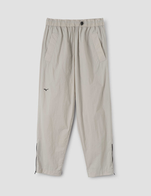 Light grey trousers with side pockets, elasticated waist with toggle cinch adjuster, black zip on hems and small black Mizuno logo, front flat lay view. 