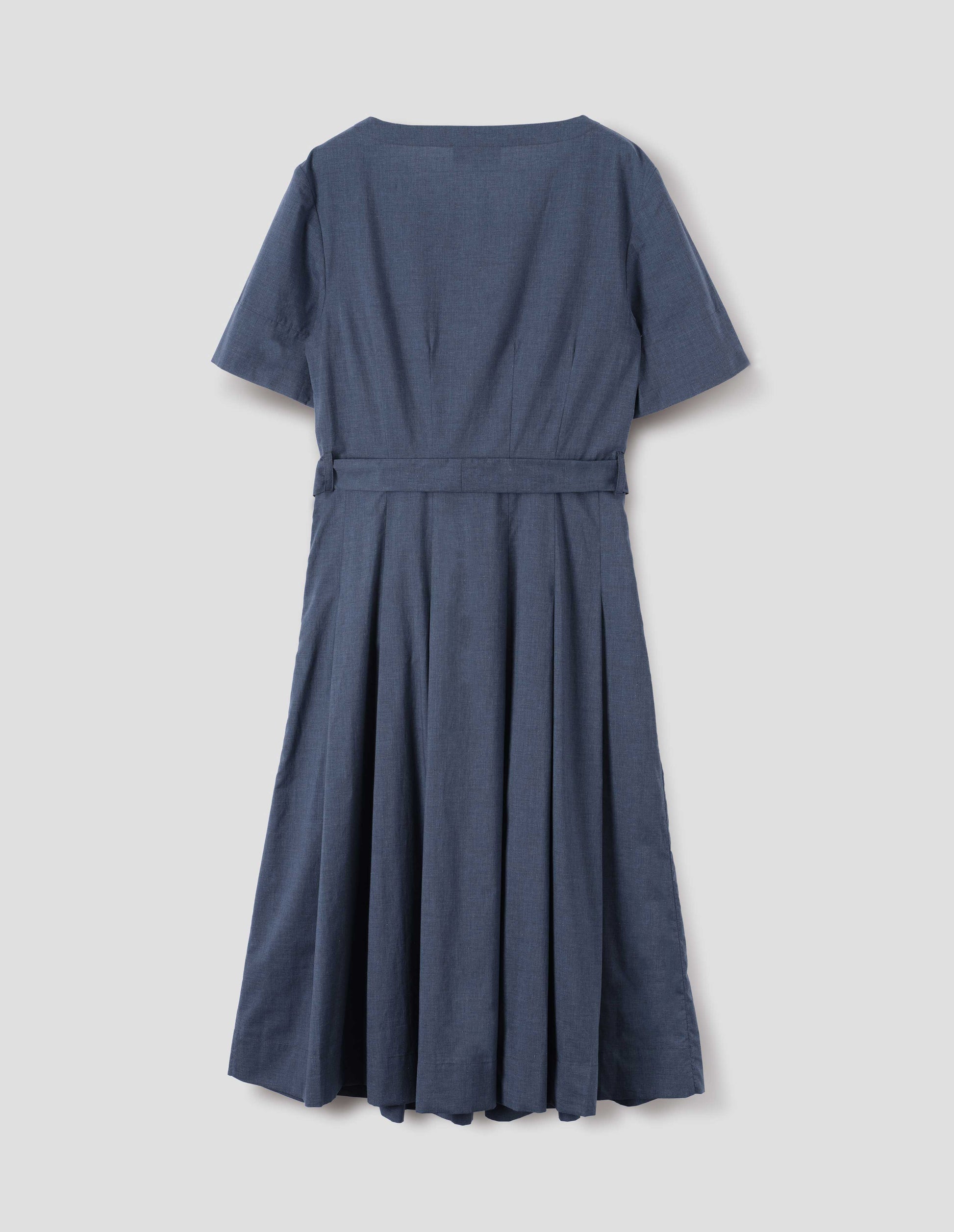 Blue cotton chambray dress, with t-shirt sleeves, deep hem, stitched down pleats, self tie, side pockets and mother of pearl button detailing on one side. Back flat lay view.