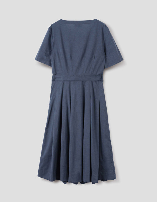 Blue cotton chambray dress, with t-shirt sleeves, deep hem, stitched down pleats, self tie, side pockets and mother of pearl button detailing on one side. Back flat lay view.