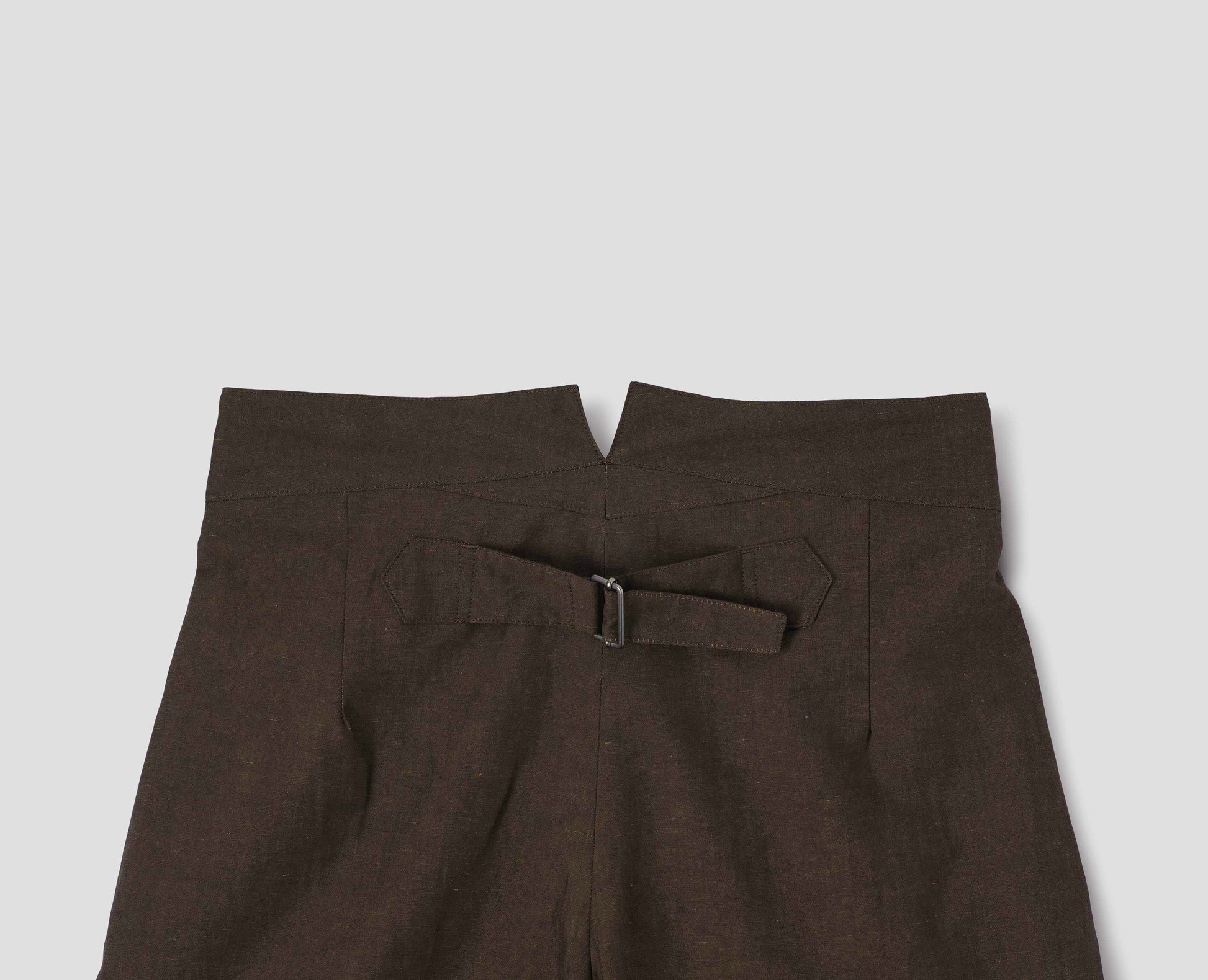 Brown cotton linen trousers, with deep waistband and cinch adjustor on centre back seam. Back flat lay view.