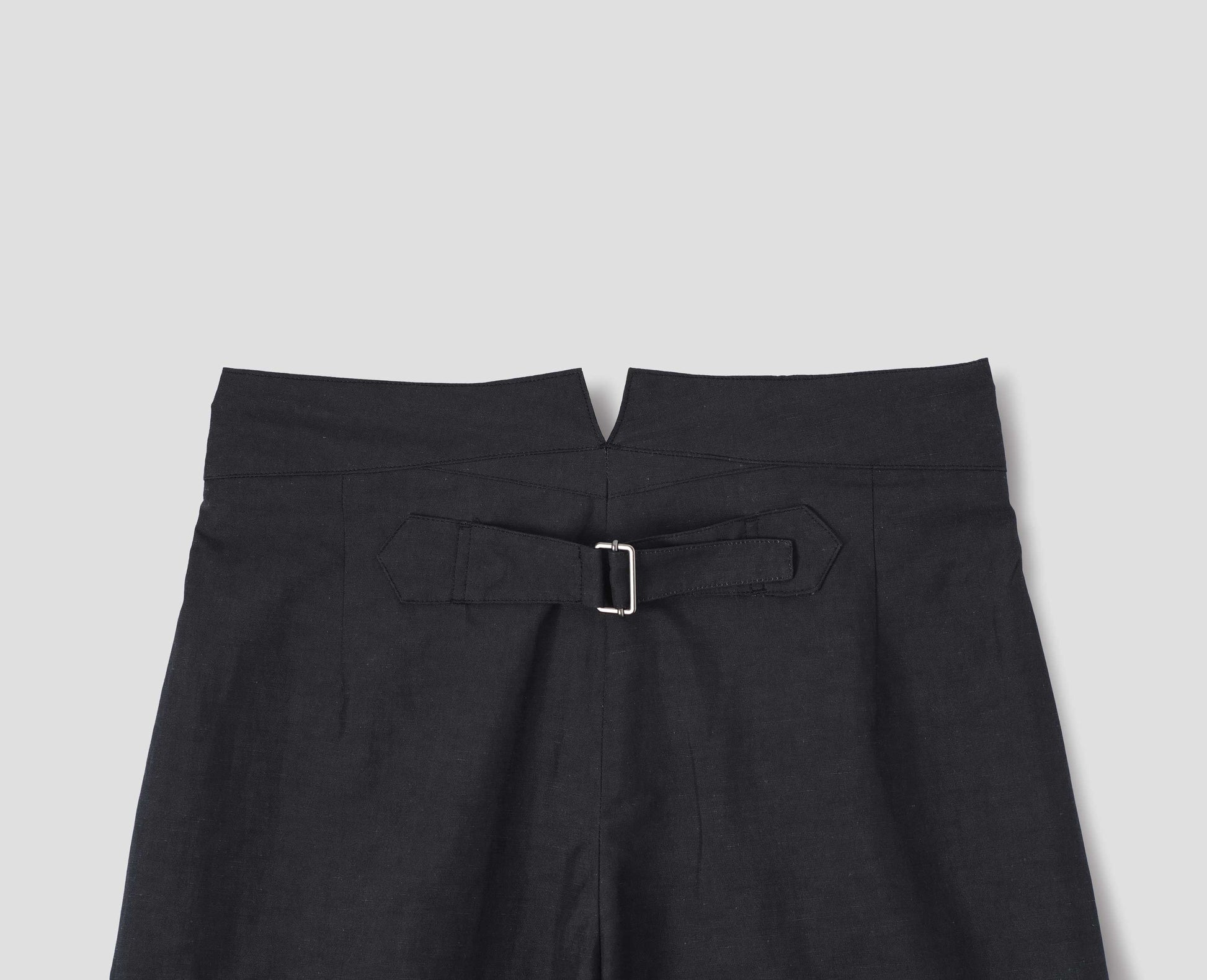 Black cotton linen trousers, with deep waistband and cinch adjustor on centre back seam. Back flat lay view.