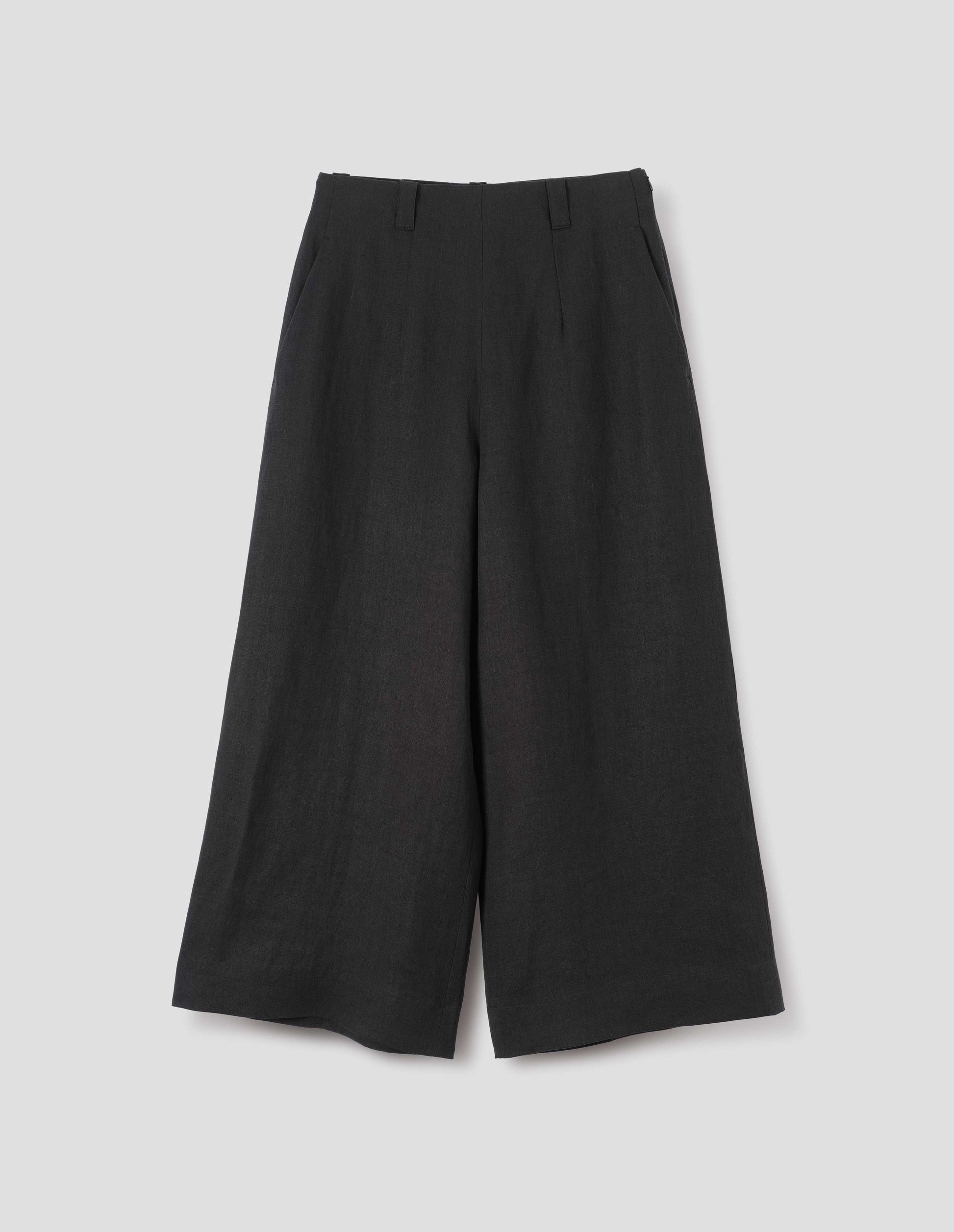 Black wide leg culottes with grown-on waistband with belt loops, concealed side zip with horn button tab fastening, and slant pockets. Front flat lay view.