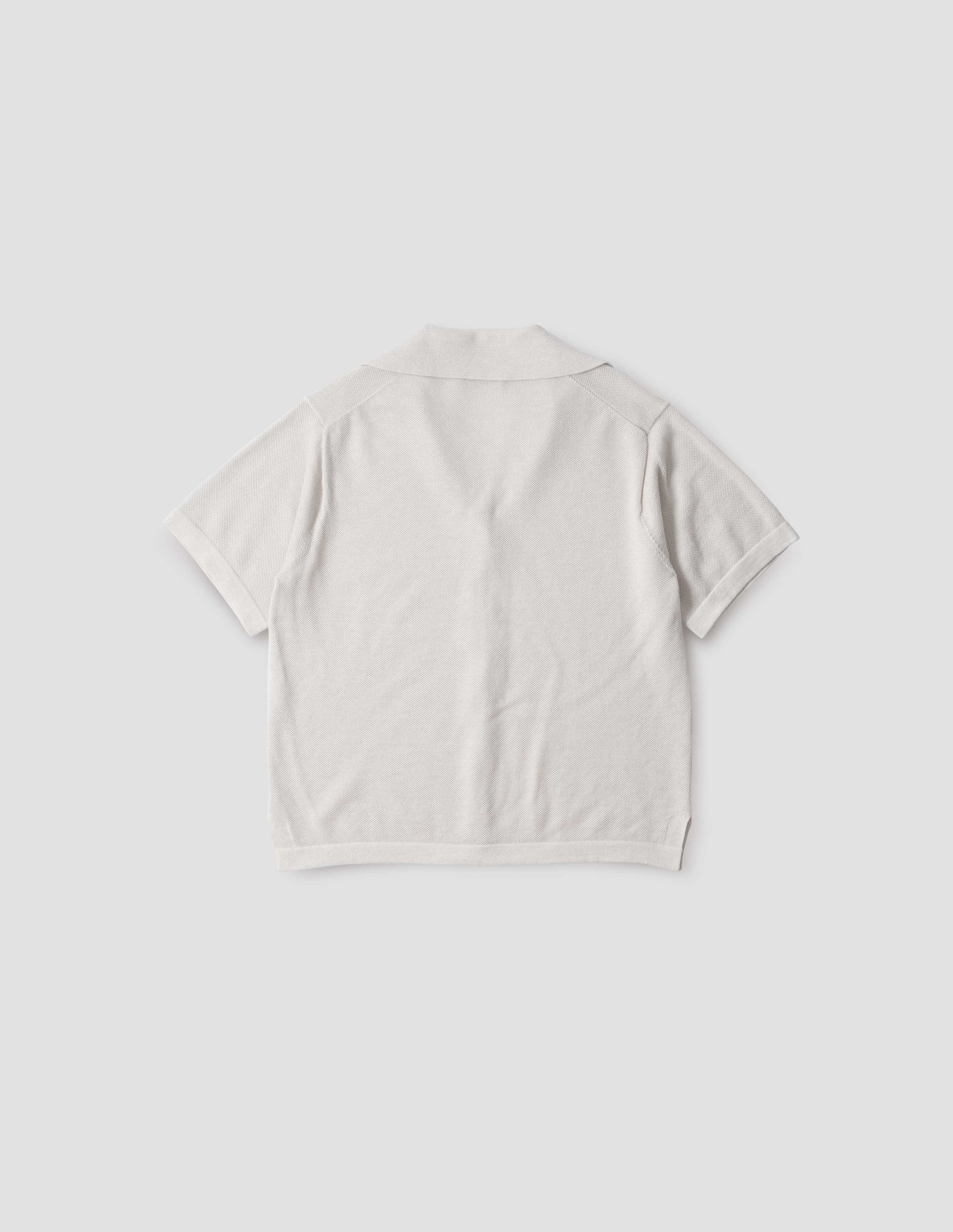 Off white knitted cotton short sleeve shirt, with fine gauge rib collar, placket, cuffs and side split hem. Back flat lay view. 