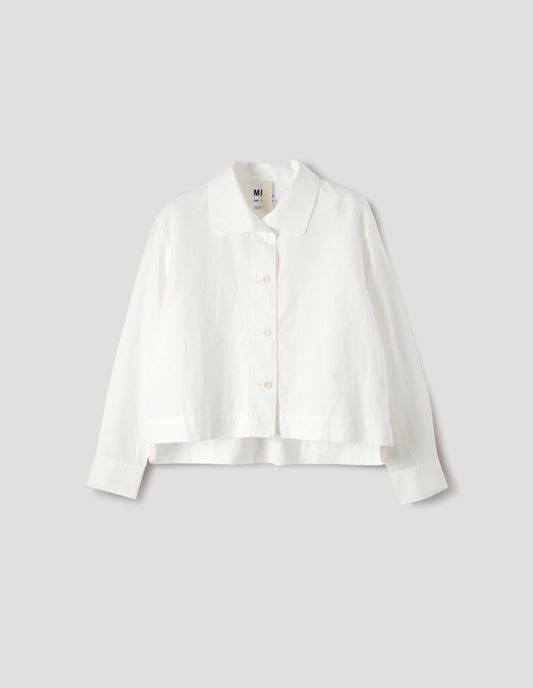 White shirt with round asymmetrical collar, wide stitch-through placket with corozo brace buttons and stepped vent split hem. Front flat lay view.