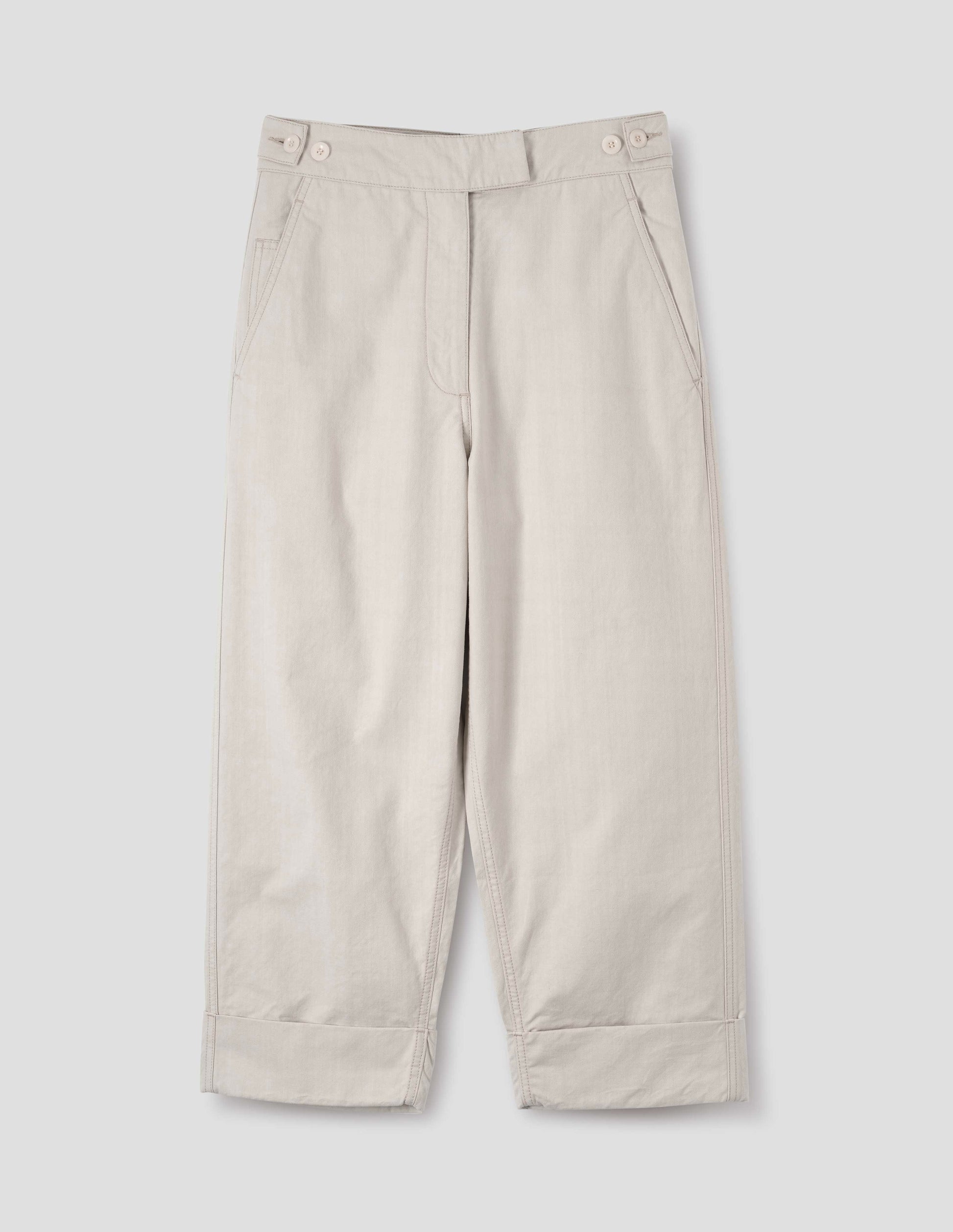Beige cotton drill trousers with slant pockets, corozo button detailing on waistband and turn up hems. Front flat lay view.