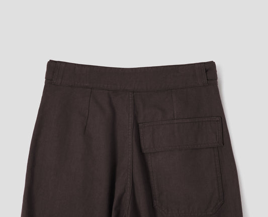 Dark brown cotton drill trousers with adjustable tab detailing on waistband and flap patch pocket. Back flat lay view.