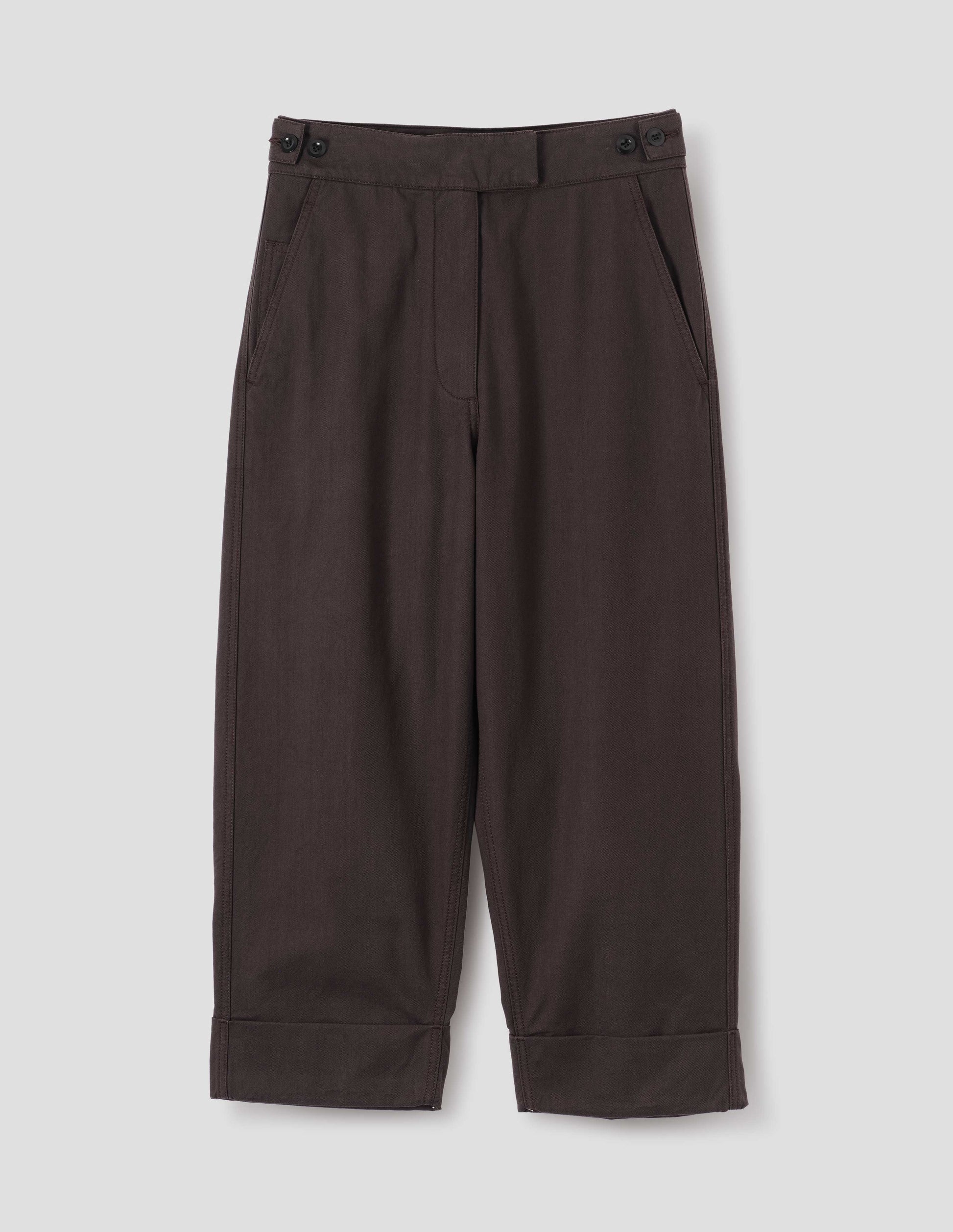 Dark brown cotton drill trousers with slant pockets, corozo button detailing on waistband and turn up hems. Front flat lay view.
