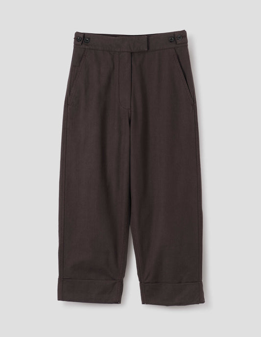 Dark brown cotton drill trousers with slant pockets, corozo button detailing on waistband and turn up hems. Front flat lay view.
