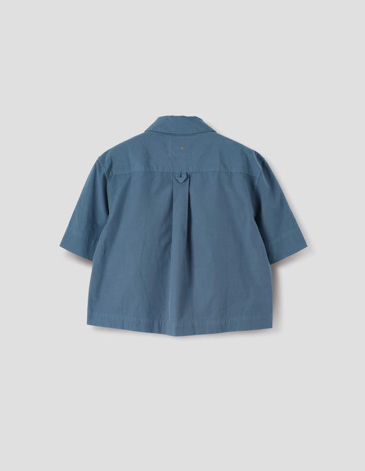 Blue cotton short sleeve shirt, with stepped side hem, hanger loop and box pleat on back yoke. Back flat lay view. 