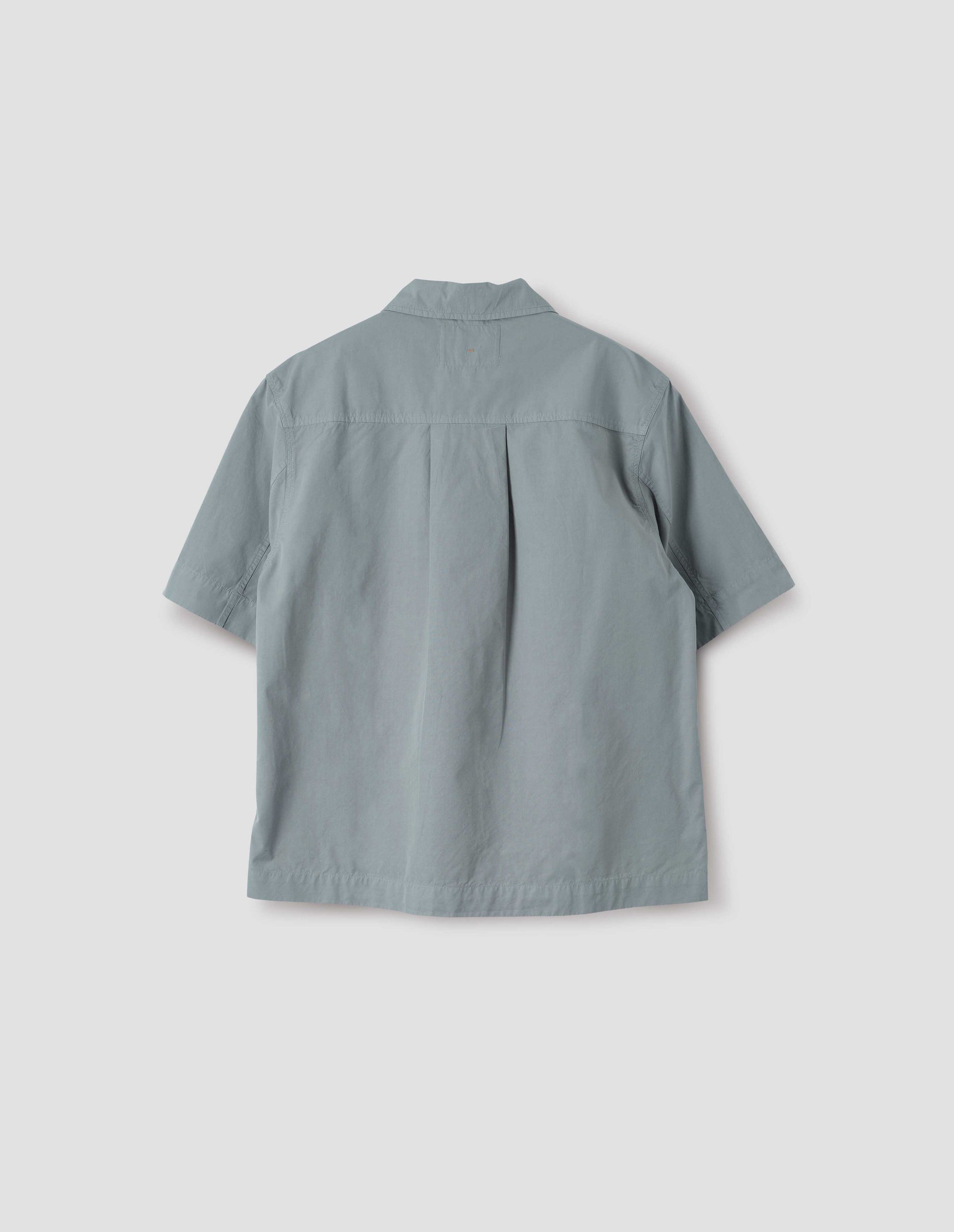 Blueish grey cotton short sleeve shirt, with side split hem and wide box pleat on back yoke. Back flat lay view.