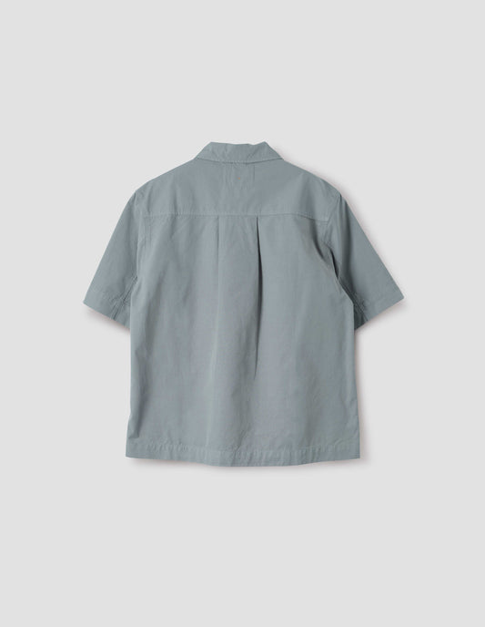 Blueish grey cotton short sleeve shirt, with side split hem and wide box pleat on back yoke. Back flat lay view.