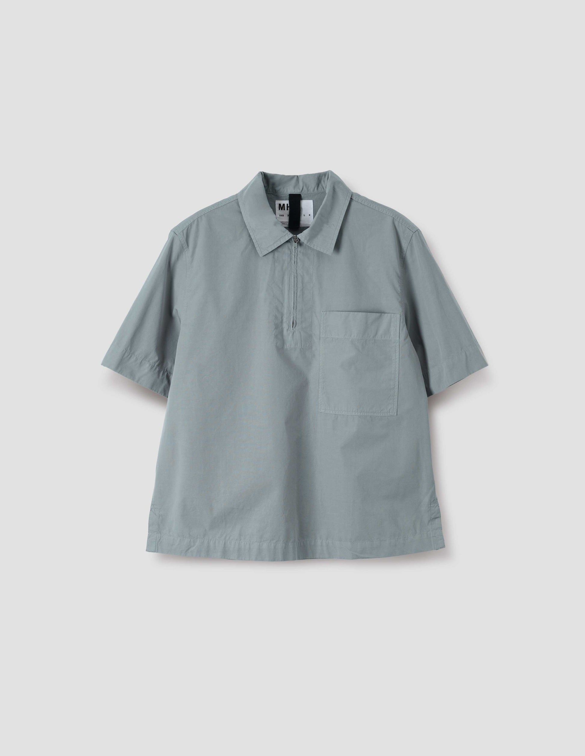 Blueish grey cotton short sleeve shirt, with wide stitch through placket, half zip, patch chest pocket and side split hem. Front flat lay view.