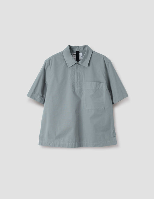 Blueish grey cotton short sleeve shirt, with wide stitch through placket, half zip, patch chest pocket and side split hem. Front flat lay view.