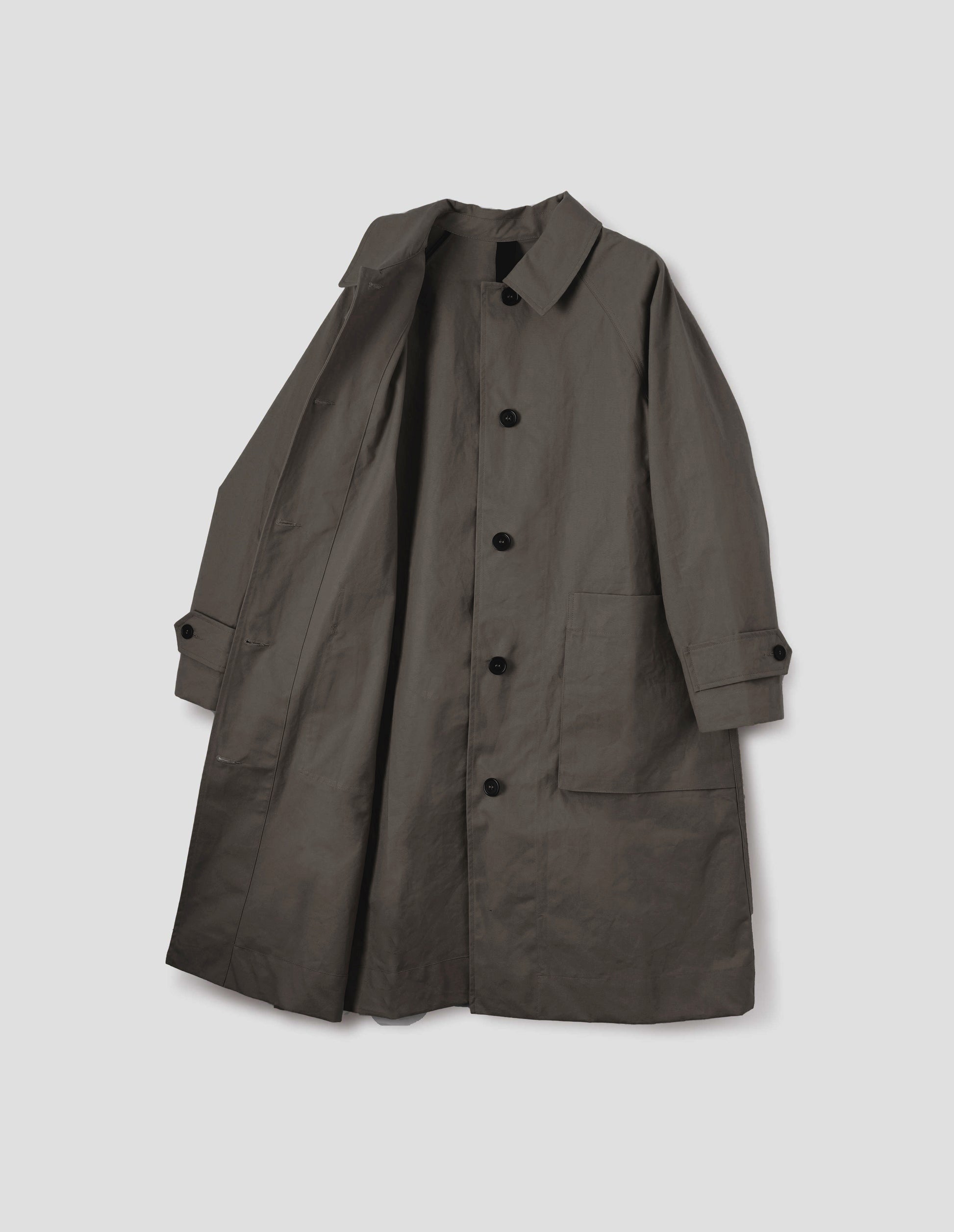 Greyish brown cotton canvas long sleeve mac, with storm tab fastening neck, raglan sleeve, button tab adjustable cuffs and large patch bellow pockets. Front flat lay open view.