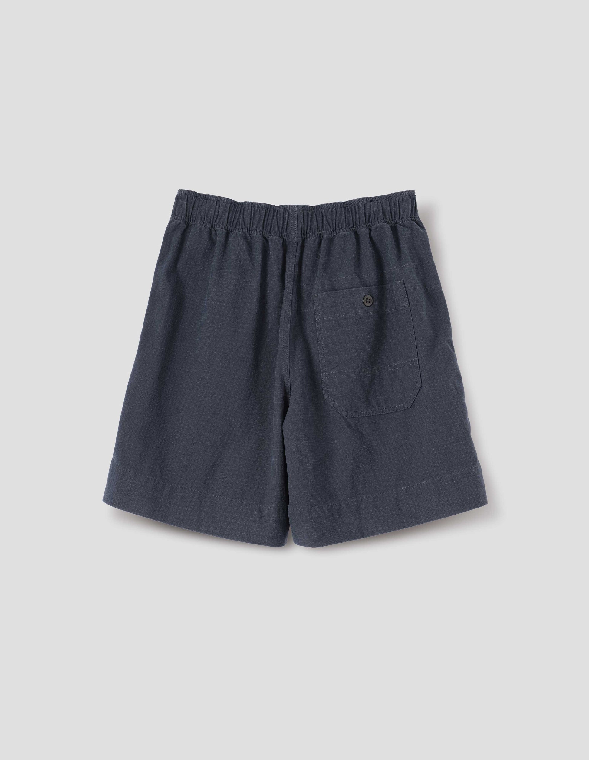 Dark navy blue cotton shorts with elasticated waist and a button-through patch pocket. Back flay lay view.