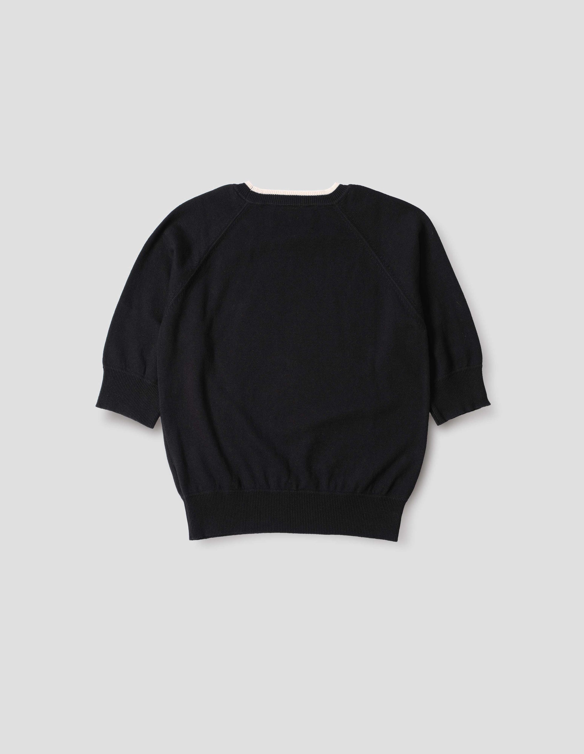 Black short sleeve knitted t-shirt, with contrast white stitching on neckline, raglan sleeve, flatlock stitch seam detailing and contrast rib on sleeve and hem. Back flat lay view.