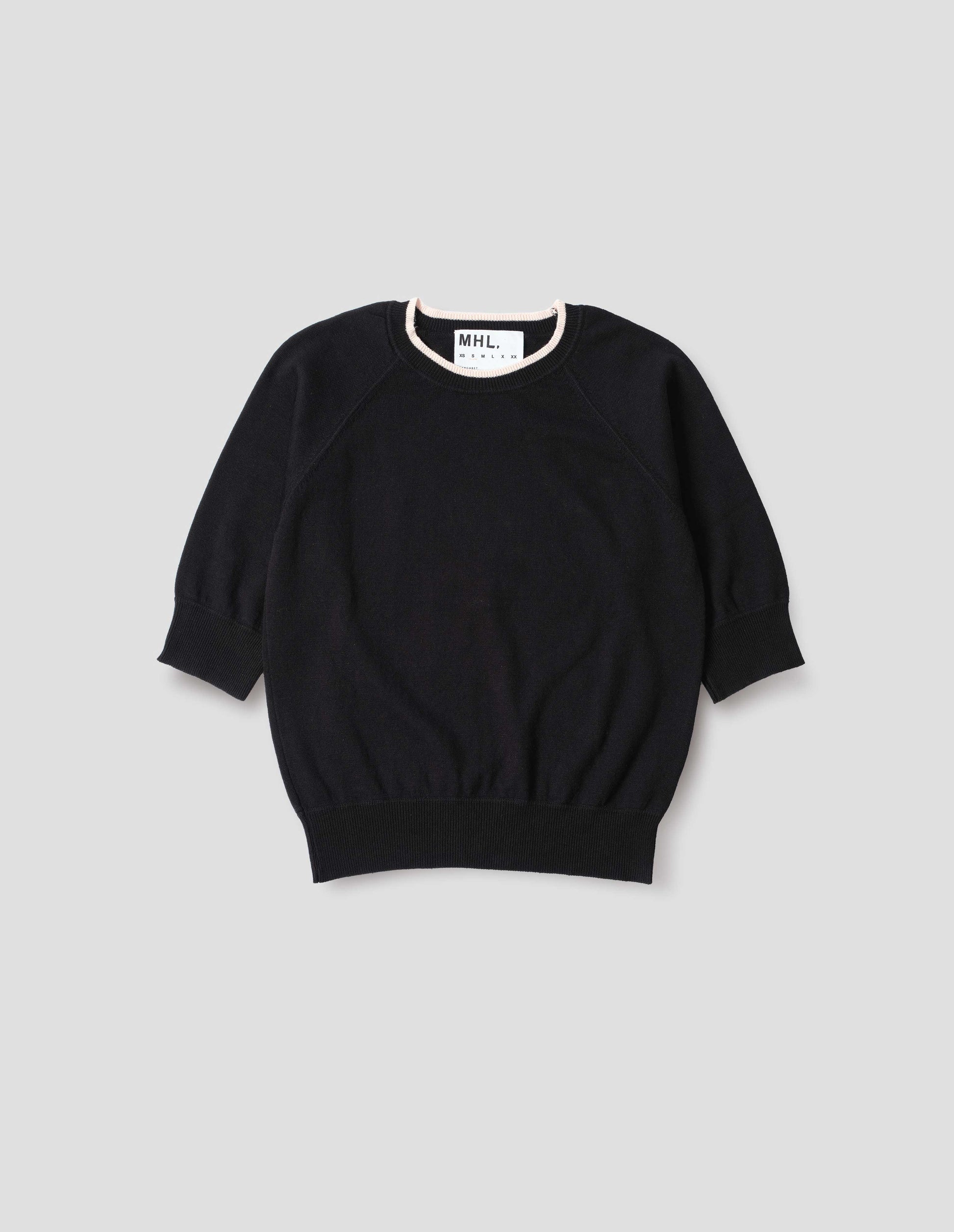 Black short sleeve knitted t-shirt, with contrast white stitching on neckline, raglan sleeve, flatlock stitch seam detailing and contrast rib on sleeve and hem. Front flat lay view.