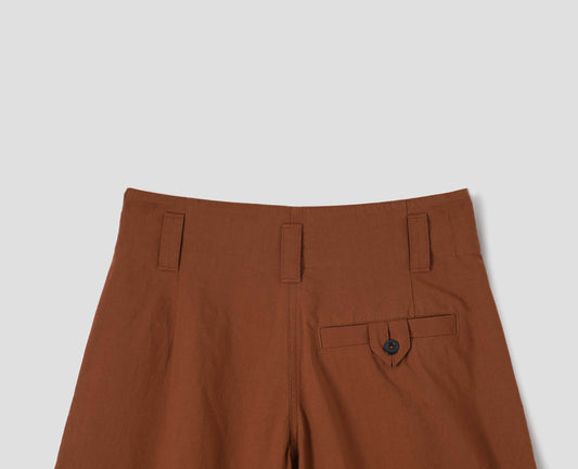 Dark orange culottes with stitch-through waistband and dropped belt loops, and corozo button loop fastening welt pocket. Back flat lay view.