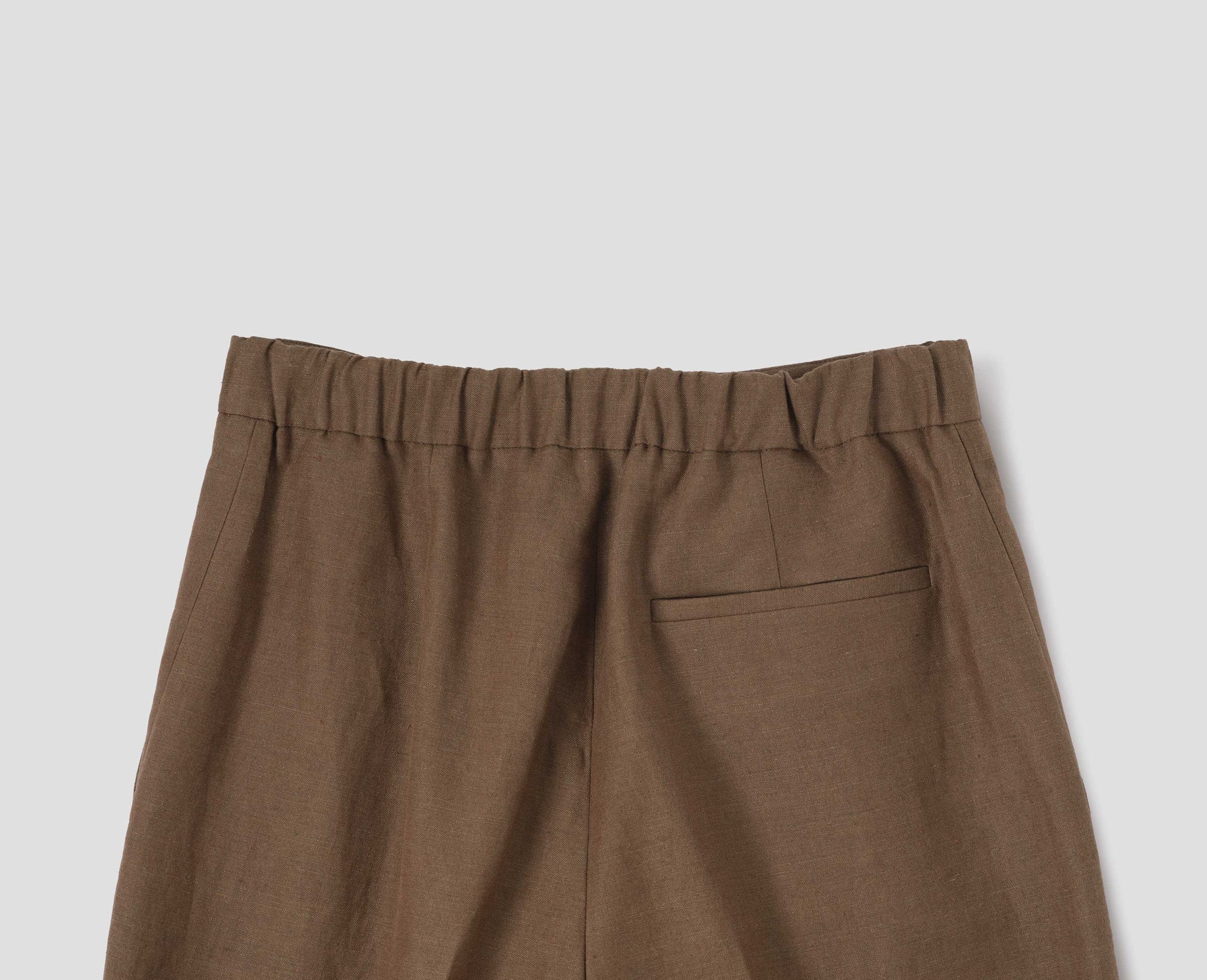 Brown linen trousers, with half elasticated waistband and belt back pocket. Back flat lay view.