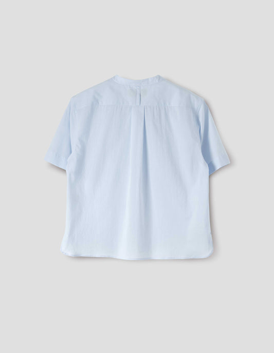 Light blue collarless shirt with short sleeves, side split stepped hem, box pleat and hanger loop detail on back yoke, and buttonhole detailing on collar band. Back flat lay view.