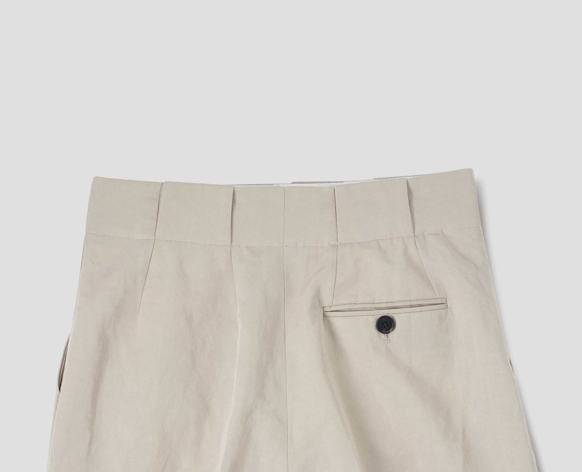 Beige cotton linen blend trousers, grown-on waistband with large belt loops and a button-through jet back pocket and horn button. Back flat lay view.