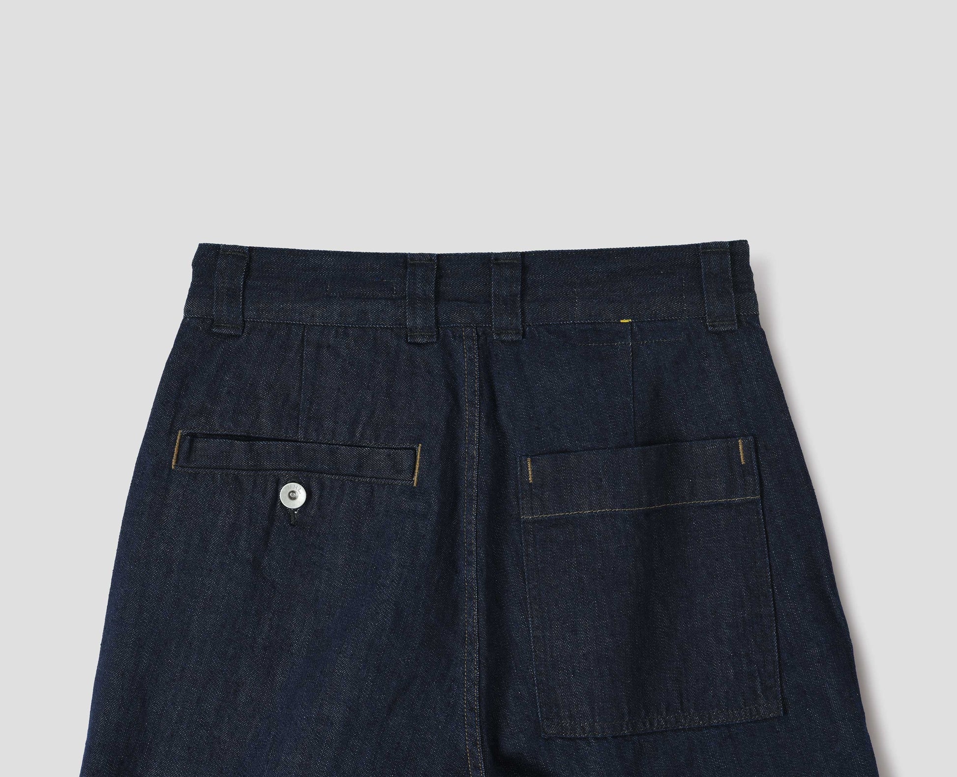 Dark blue denim twill trousers with high waist, belt loops, metal button-through welt and patch back pocket. Back flat lay view. 