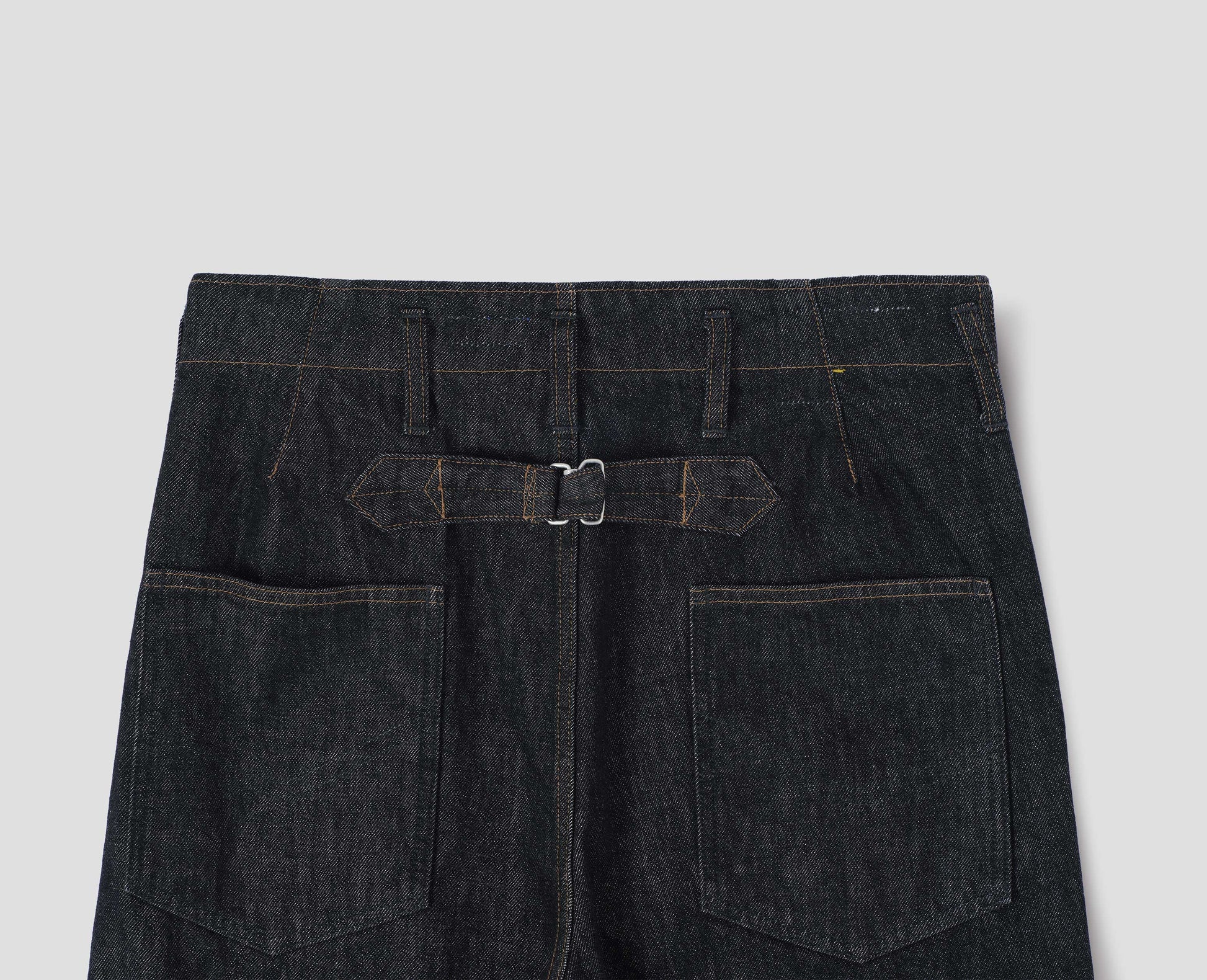 Black denim twill jeans, with stitch-through waistband with belt loops, cinch back detail with metal buckle and patch back pockets. Back flat lay view.