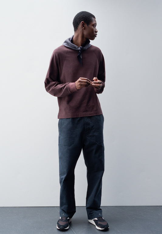 Full body image, front view of male model wearing grey wool scout scarf with dark navy wool trim. Styled with burgundy long sleeve t-shirt, blue trousers and brown and black trainers.