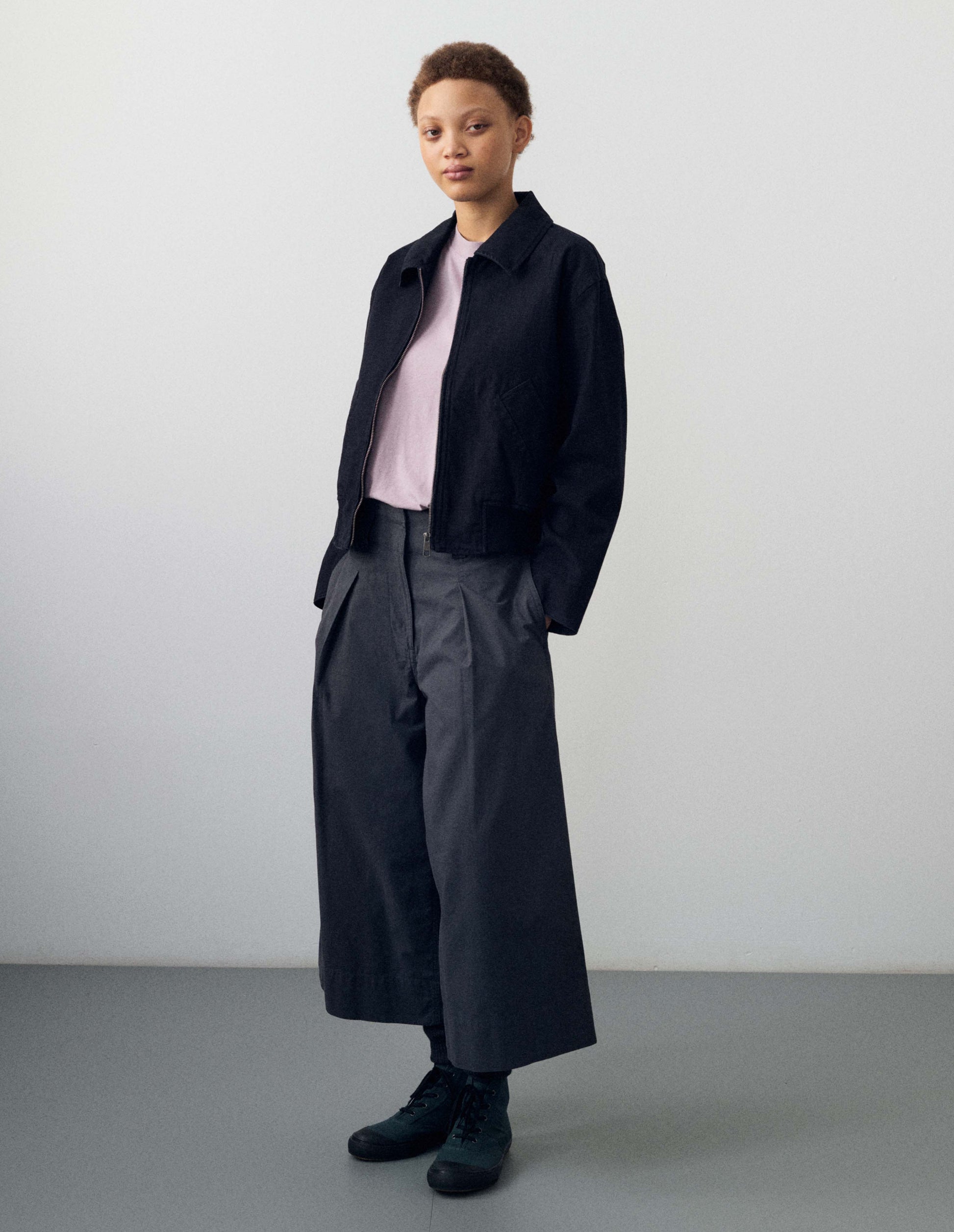 Full body image, front view of model wearing lilac cotton linen long sleeve t-shirt with contrast rib on neckline and raglan sleeve detailing. Styled with dark navy blue long sleeve zip up shirt, dark navy blue culottes, black socks and dark blue shoes with black gum soles.